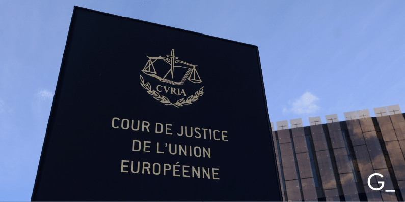 The image shows the exterior of the Court of Justice of the European Union (Cour de Justice de l'Union Européenne). The sign features the emblem of the European Court of Justice with the scales of justice symbol and the abbreviation CVRIA. The building appears modern with a glass facade and is set against a clear blue sky.